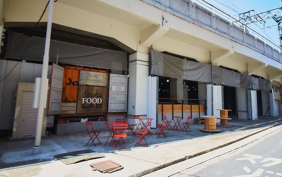 OSAKA FOOD LAB 外観 阪急線の高架下に並ぶ赤い椅子とテーブル